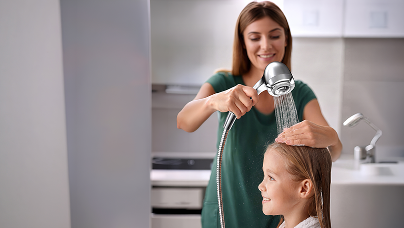 Woman washing little girl's hair with shower head