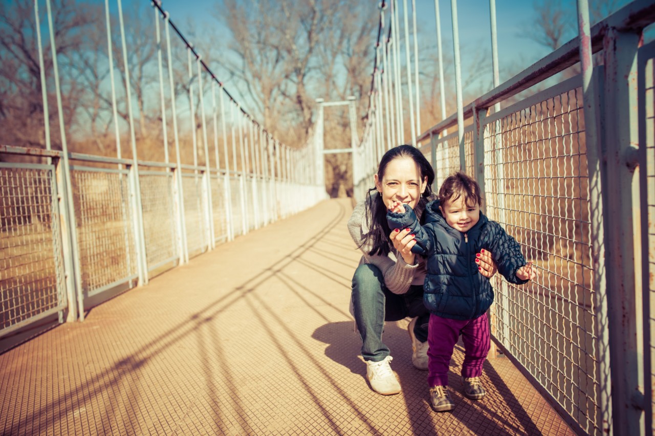 Young mother playing with baby daughter on footbridge